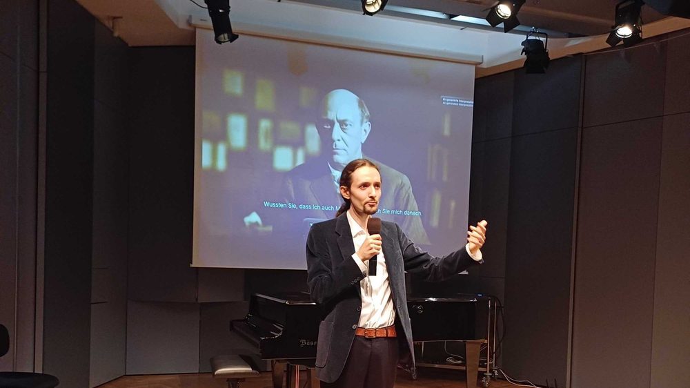 Célest Lang präsentiert ComposerMeet im Arnold Schönberg Center, dahinter der KI-Avatar von Arnold Schönberg